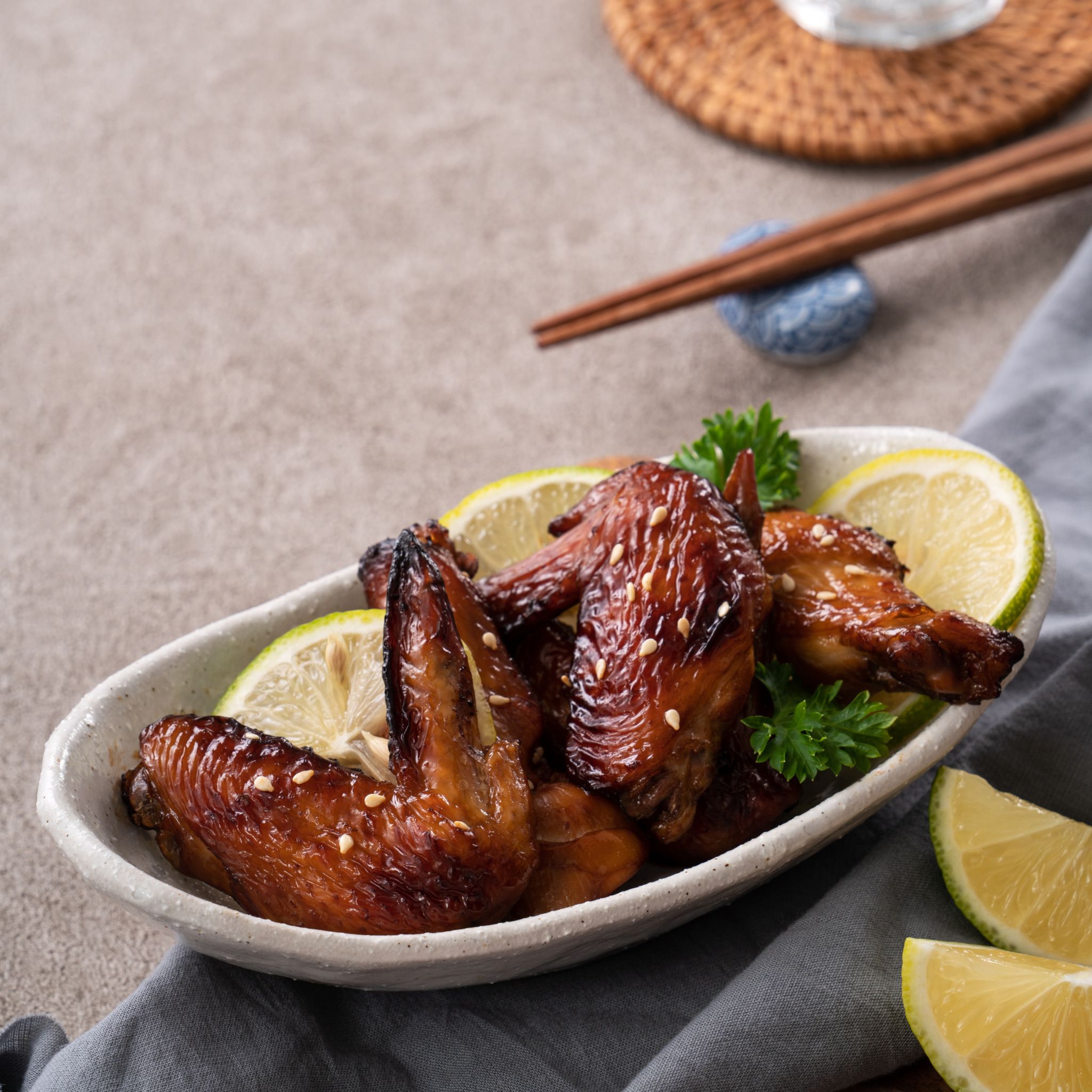 Close up of roasted sweet sauced teriyaki chicken wings in a white plate on gray table background.